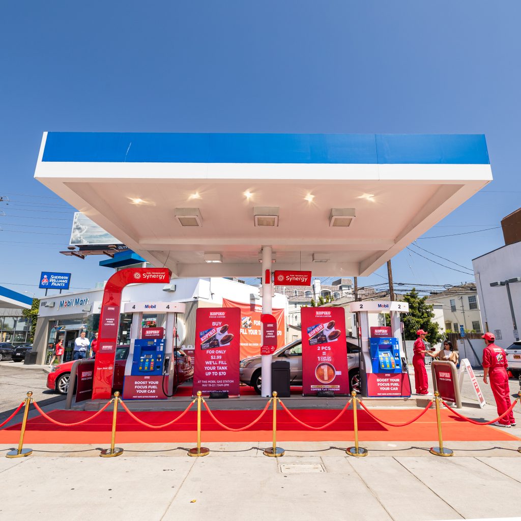 The Mobil gas station near UCLA is decked out in red Kopiko branding, with red carpets and red and gold stanchions. Attendants in red jumpsuits stand by pumps to direct cars where to go.