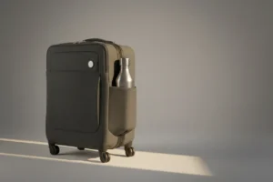 Minimalist carry-on suitcase with a stainless steel reusable water bottle against a soft neutral background.