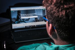Close-up of a person using a laptop to browse stock photos online in dim lighting