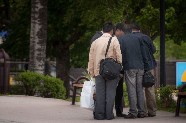 A group of men standing together in an outdoor park setting, engaged in discussion