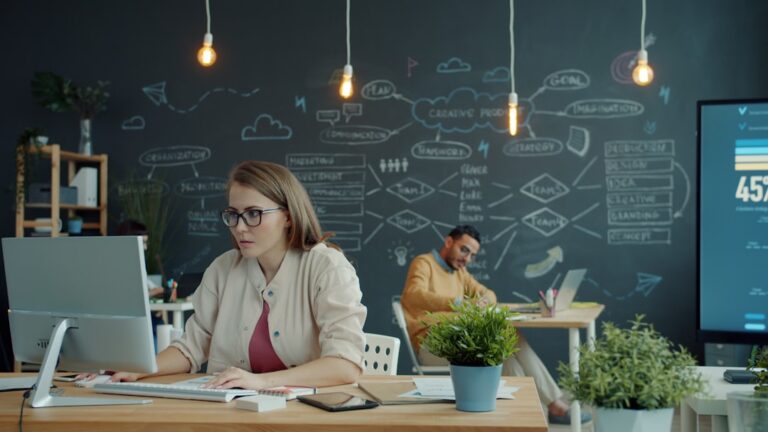 A person thoughtfully reviews data on a tablet, surrounded by modern office technology