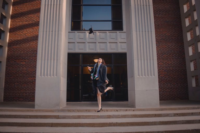 A graduate tosses a cap on the steps of a university building after finishing a degree program.