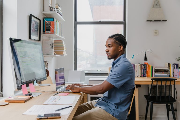 A professional man working on a laptop and computer in a stylish home office setting