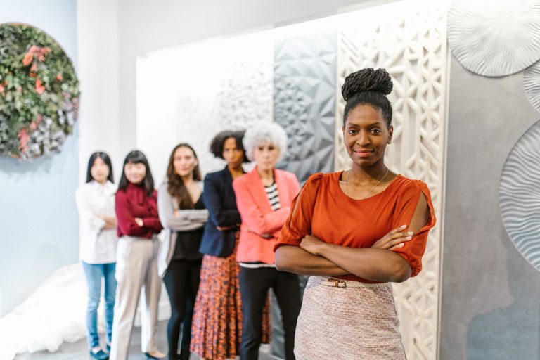 A confident female leader stands with diverse female colleagues in a modern office setting