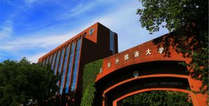 The red-brick gate and main building of Beijing Foreign Studies University under a blue sky with trees.