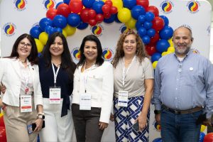 Five smiling attendees pose together under a red, blue and yellow balloon arch at a Hispanic Unity of Florida Entrepreneur Summit.