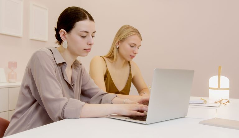 Two women work together at a laptop in a bright office