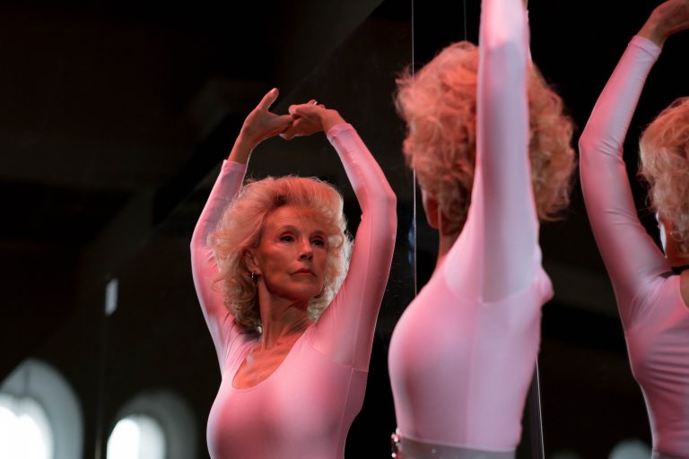 A graceful senior woman in a leotard dancing ballet indoors, showcasing elegance