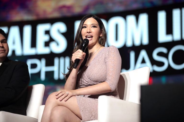 Lauren Chen seated in a pink dress speaking into a microphone