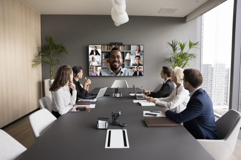 Executives meet around a conference table with remote colleagues on screen