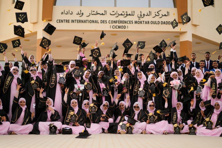 Group of graduates celebrating outside a conference center with caps thrown in the air