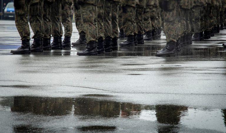 Soldiers in camouflage trousers and black boots standing on wet pavement