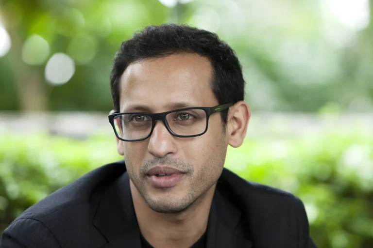 Portrait of Nadiem Makarim wearing black glasses against a blurred green background